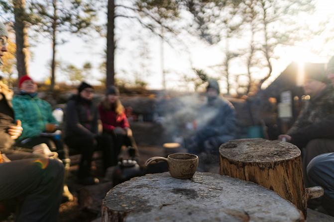 Kannon päällä kuksa, jossa on höyryävää juomaa. Taustalla on ryhmä ihmisiä.