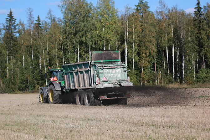 Kuvassa on traktori, joka levittää pellolle kompostoitua rakennekuitua. 