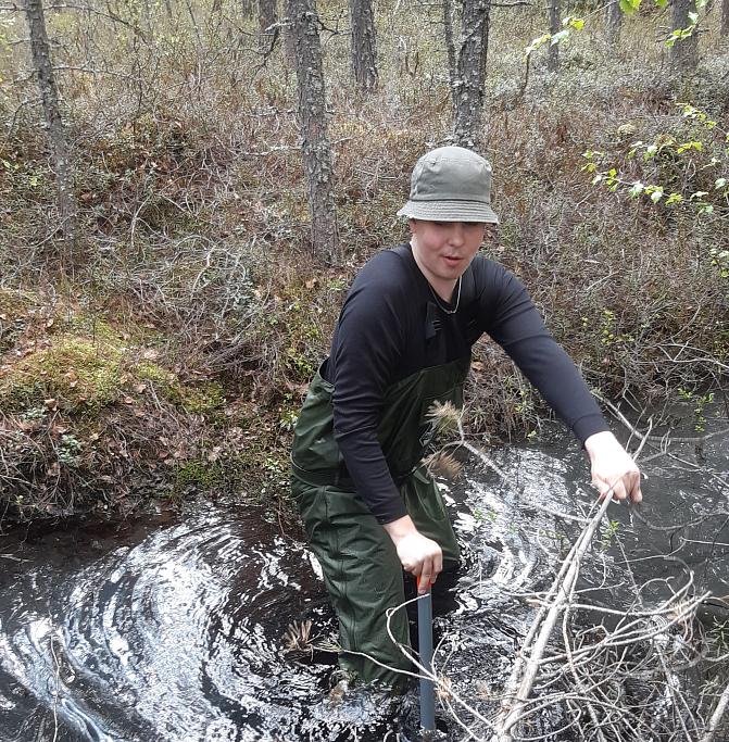 Aleksi Isoaho ylittämässä veden täyttämää ojaa kahluusaappaat yllään.