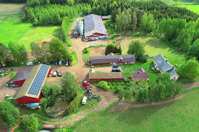 Ilmakuvaa maatilasta. Useita rakennuksia, joista etualan katolla aurinkopaneelit. 