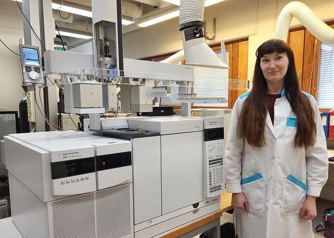 Tutkija valkoisessa takissa seisoo tutkimuslaitteiston vieressä laboratoriossa