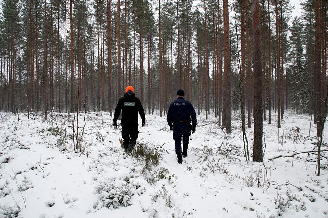 Poliisi ja erätarkastaja kävelevät metsäisessä maisemassa.