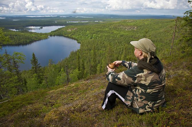 ihminen istuu katselemassa alhaalla avautuvaa luontomaisemaa
