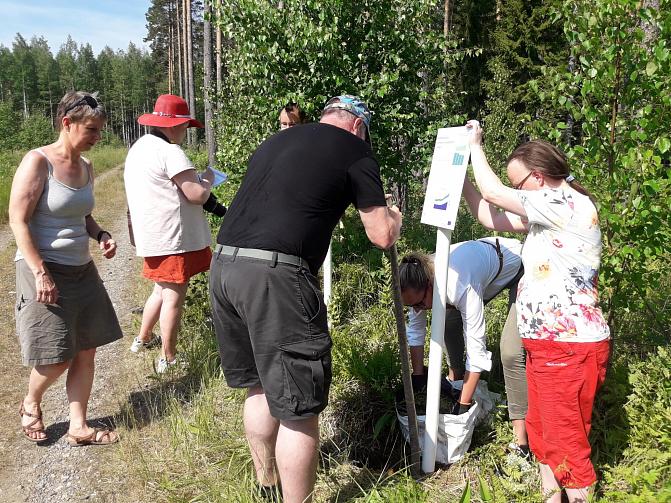 Kuvassa viisi henkilöä pystyttää opastaulua Punkaharjun tutkimuspuistossa.